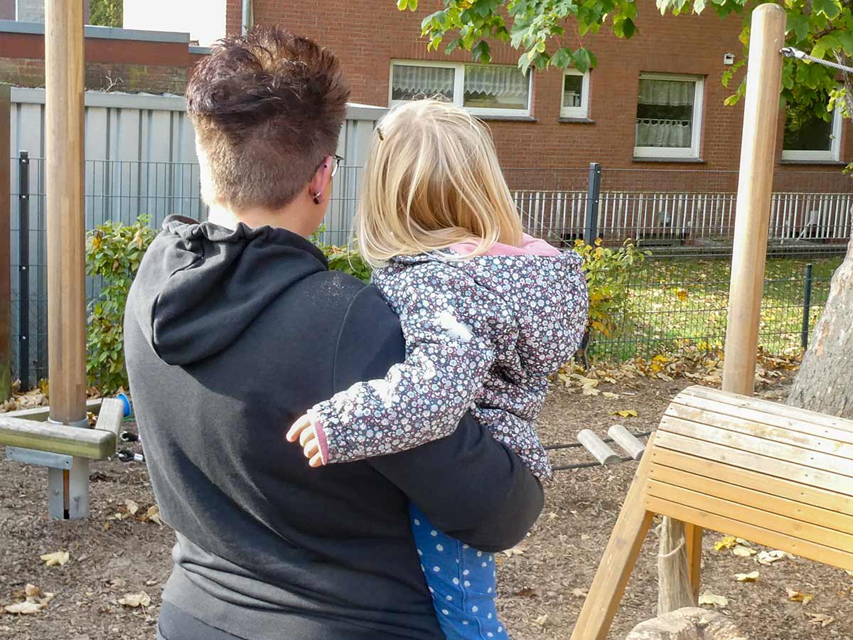 Kita Bärenhöhle: Erzieherin mit Kind auf dem Arm, Spielplatz