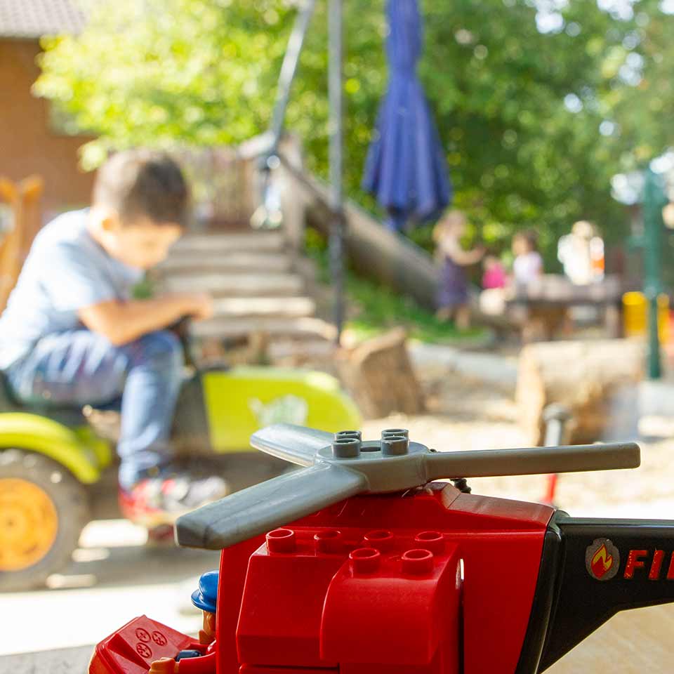 Kita Bärenhöhle: Spielzeug im Vordergrund, Junge auf einem Trampeltrecker 